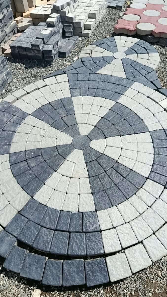 Grey and charcoal circle-kit cabro laid out on the yard floor, with pallets of stock paving blocks behind